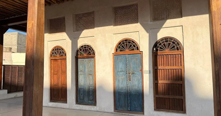 أبواب خشبية قديمة منحوتة داخل فتحات مقوّسة في بيت من الحجر المرجاني على مسار اللؤلؤ في المحرق